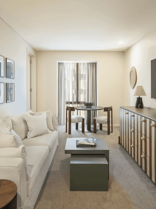 Modern hotel suite living room with white sectional sofa, framed artwork gallery wall, and dining area