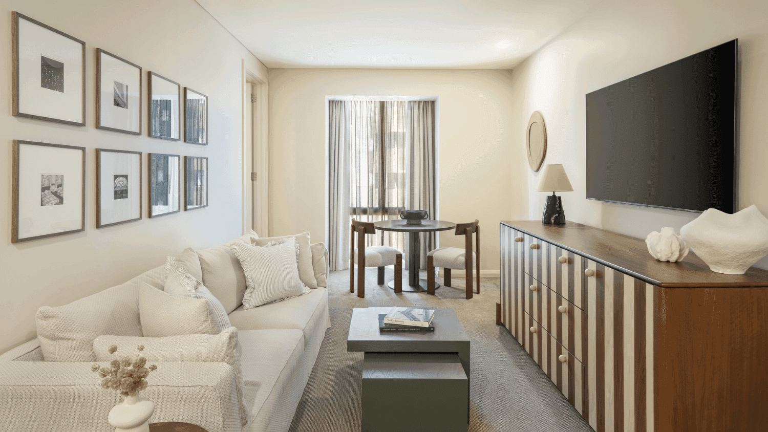Modern hotel suite living room with white sectional sofa, framed artwork gallery wall, and dining area