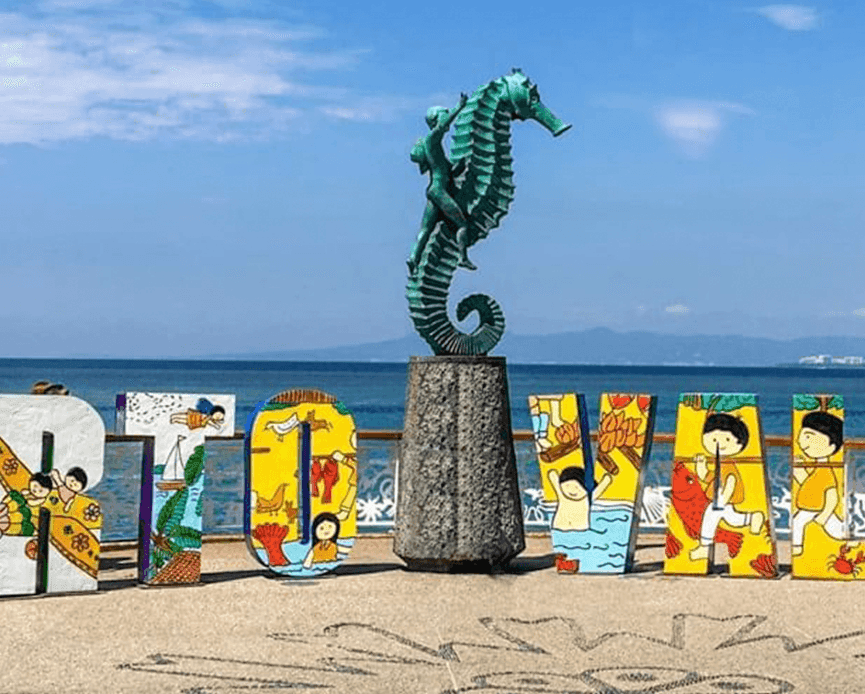 The iconic bronze seahorse statue next to the colorful Puerto Vallarta sign on a sunny beach boardwalk near Casa Dona Susana