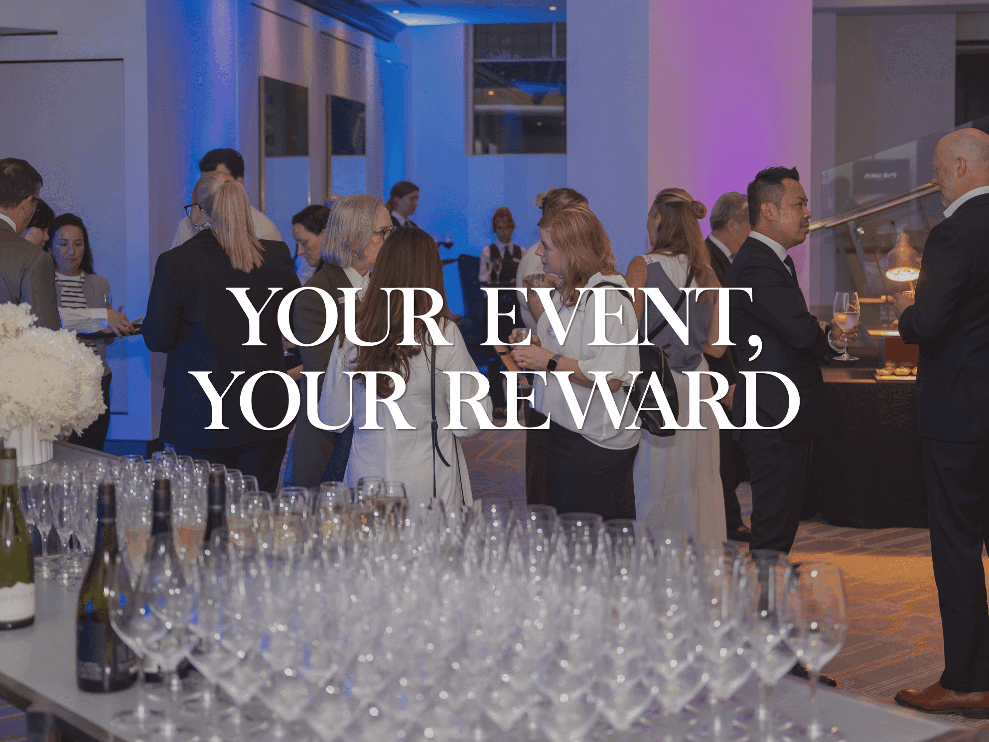 Elegant event space with guests mingling near wine glasses and ambient blue and purple lighting for special occasions.