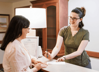 Spa receptionist assisting a guest with paperwork by the front desk under a lamp at Rodd Crowbush Golf & Beach Resort