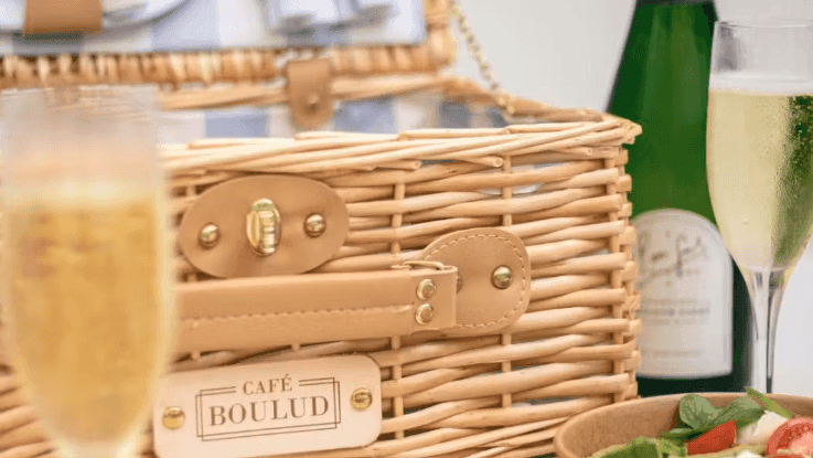 Wicker picnic basket with champagne bottle, glasses, and fresh salads arranged for an outdoor dining experience