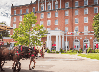 Two brown horses pulling a cart by a paved driveway under a cloudy sky near Rodd Charlottetown Hotel