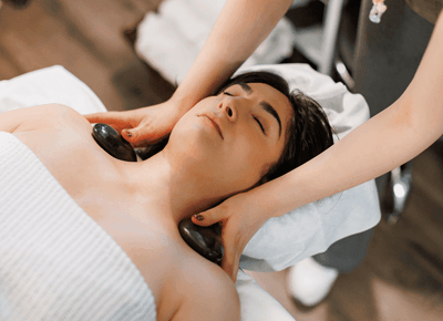 Guest receiving a hot stone neck massage by a therapist while resting on spa bed at Rodd Crowbush Golf & Beach Resort