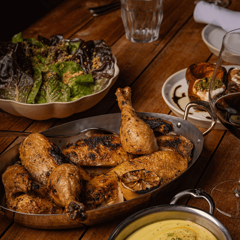 Roasted chicken with charred skin served alongside fresh salad and sides for Sunday Supper at The Drexel
