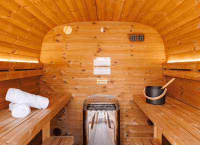 Wooden barrel sauna with bench towels beside an electric heater and a water bucket for guest wellness at Rodd Moncton
