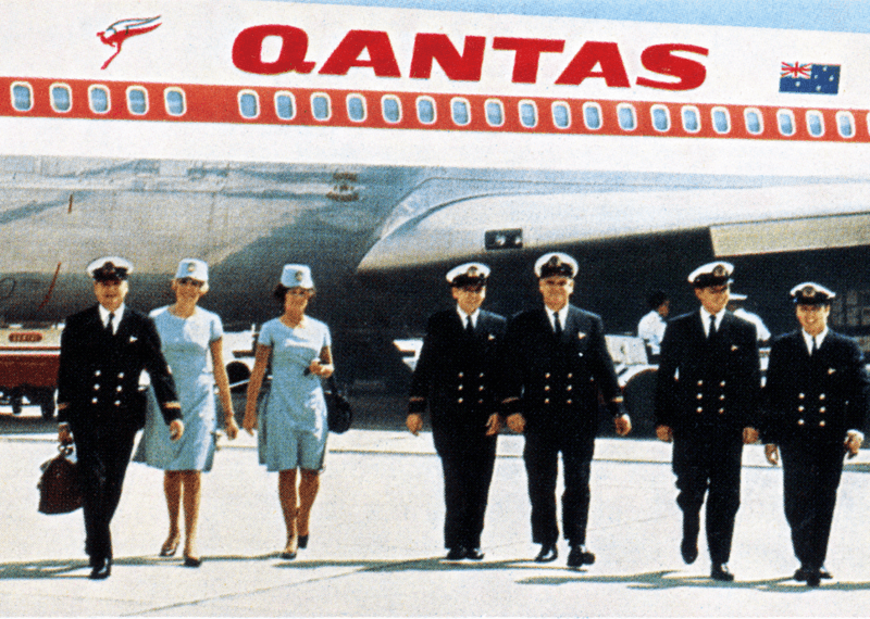 Group of Qantas flight crew and passengers walking in front of a large white plane.