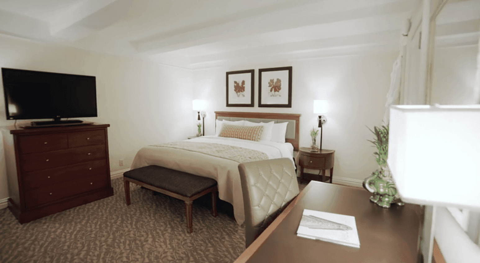 A wide view of a hotel room with a bed, dresser, desk, and TV.
