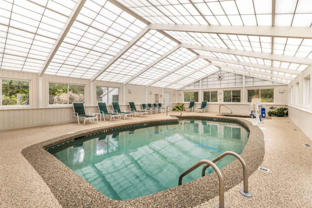 An indoor pool with a glass roof and lounge chairs around it.