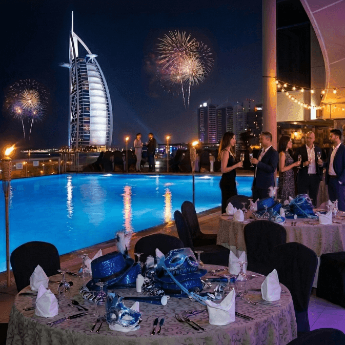 Guests celebrating New Year's Eve Gala Dinner near a pool with fireworks in the background.