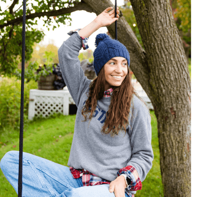 Woman sitting on a tree swing with cozy beanie outfit and green foliage background at La Tourelle Hotel and Spa