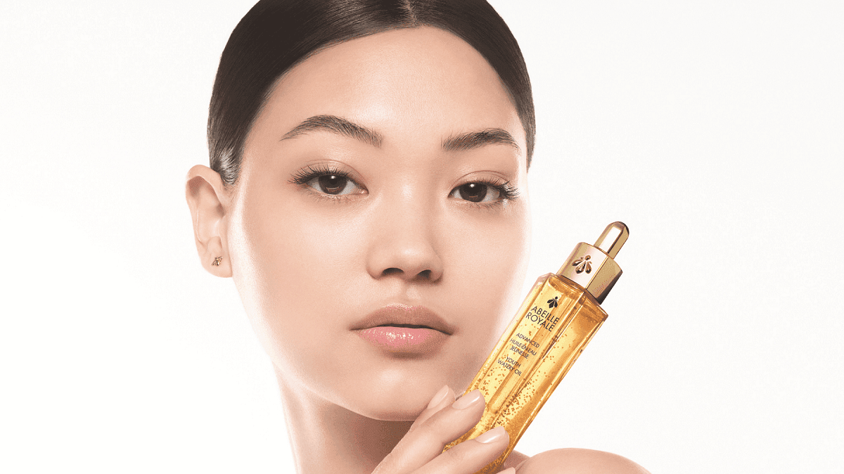 Woman holding Guerlain Abeille Royale facial oil bottle beside her face for spa advertisement at Hotel X Toronto
