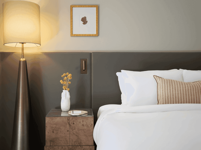 Striped pillow on a white bed by a tall lamp under a gold-framed art piece in the guest room at Sofitel Sydney Wentworth