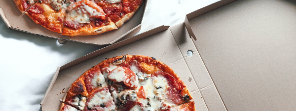 Two pizzas with melted cheese and toppings in open pizza boxes featuring Solo Takeaway at Novotel Sunshine Coast Resort