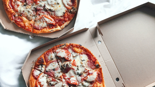 Two pizzas with melted cheese and toppings in open pizza boxes featuring Solo Takeaway at Novotel Sunshine Coast Resort