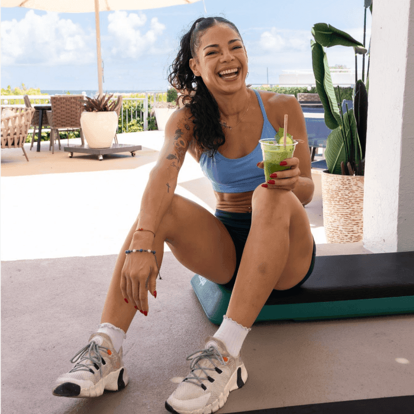Woman sitting on yoga mat holding a green smoothie in Boot Camp at The Savoy Hotel & Beach Club