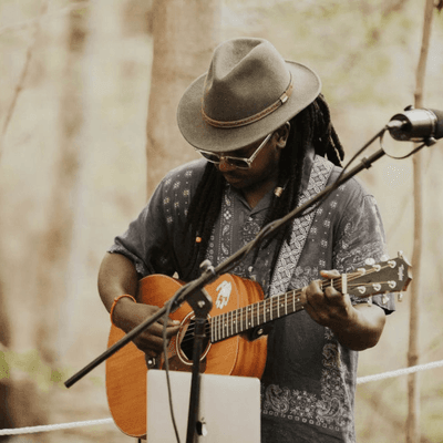 Musician wearing a hat playing acoustic guitar near a microphone outdoors at La Tourelle Hotel and Spa