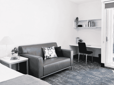 Modern student living space with gray sofa, desk area, and balcony access at Student Living - Waymouth