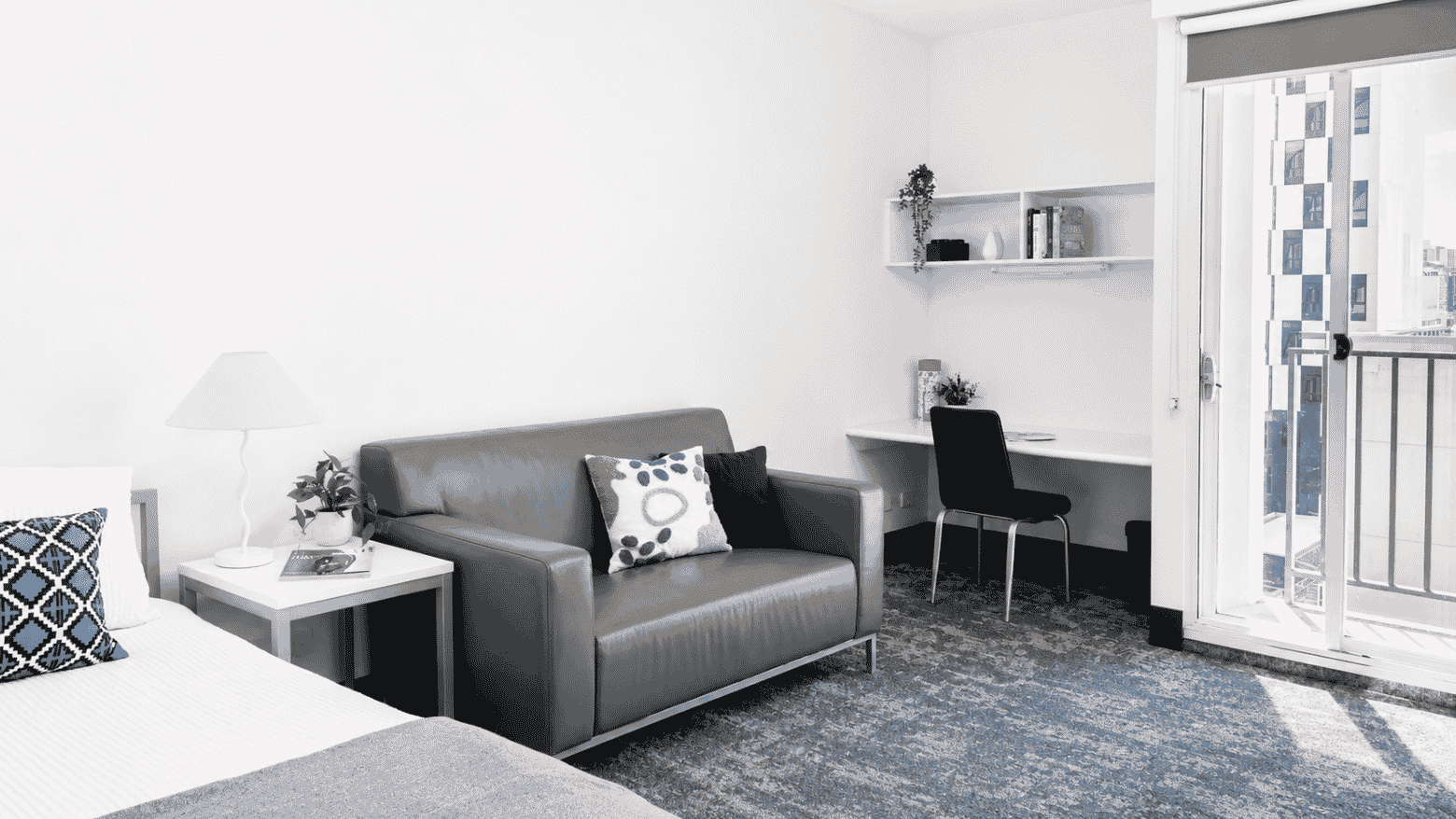 Modern student living space with gray sofa, desk area, and balcony access at Student Living - Waymouth