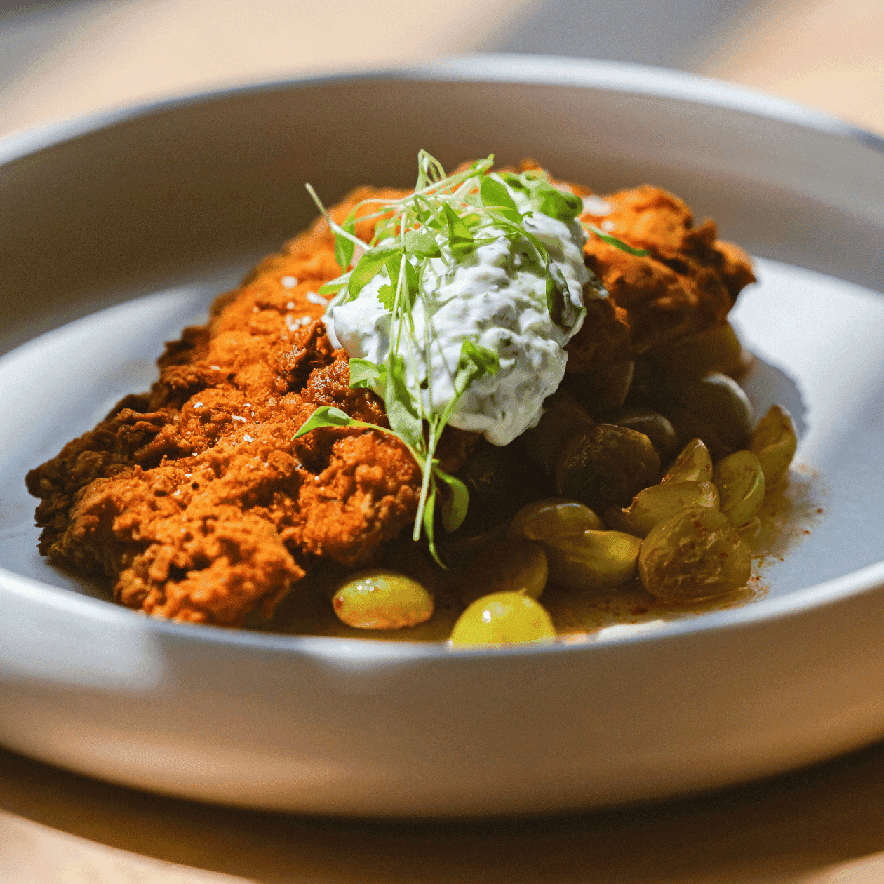 A dish with fried food, creamy sauce, and green garnish on a white plate.