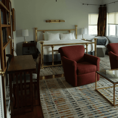 Brass bed and armchairs set on patterned area rugs near wooden writing desk inside La Tourelle Hotel and Spa suite