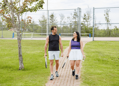 Couple carrying tennis rackets and water bottles along a path beside the courts at Rodd Crowbush Golf & Beach Resort