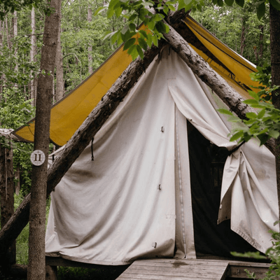 Glamping canvas tent framed by wooden poles and lush green forest trees behind at La Tourelle Hotel and Spa