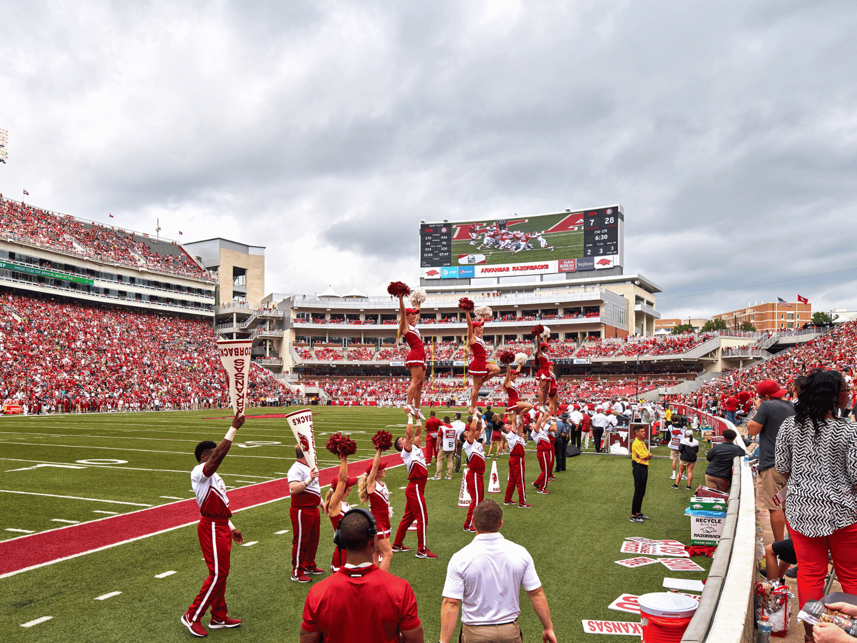 Cheerleaders perform a pyramid stunt on the football field while the crowd watches from the stands.