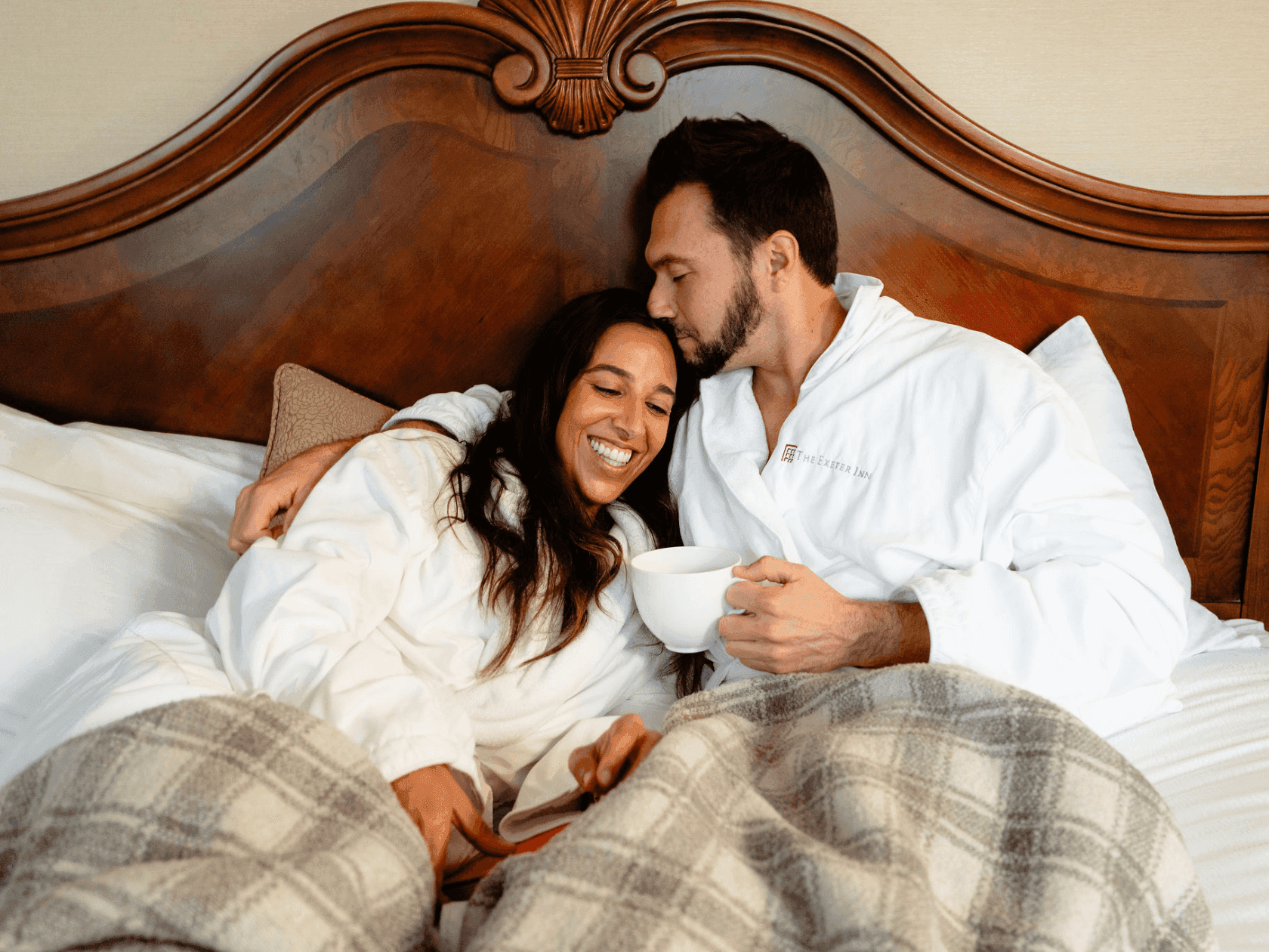 Couple relaxing in bed with a cup of coffee in the Snooze and Savor offer.