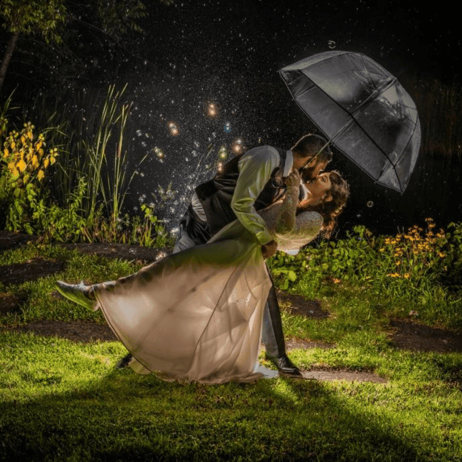Bride and groom kissing under a clear umbrella surrounded by rain and sparkling lights at La Tourelle Inn and Spa