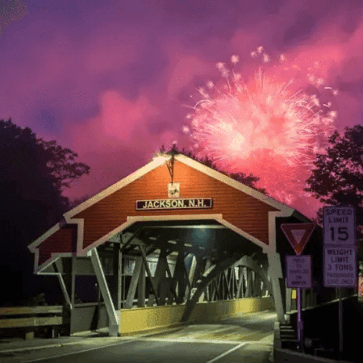 Jackson, N.H. covered bridge with fireworks display and speed limit 15 sign at night.