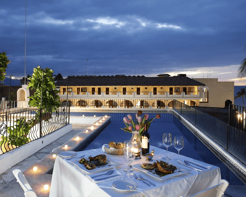 Evening rooftop dining with a set table of food and wine beside the glowing pool at Casa Dona Susana