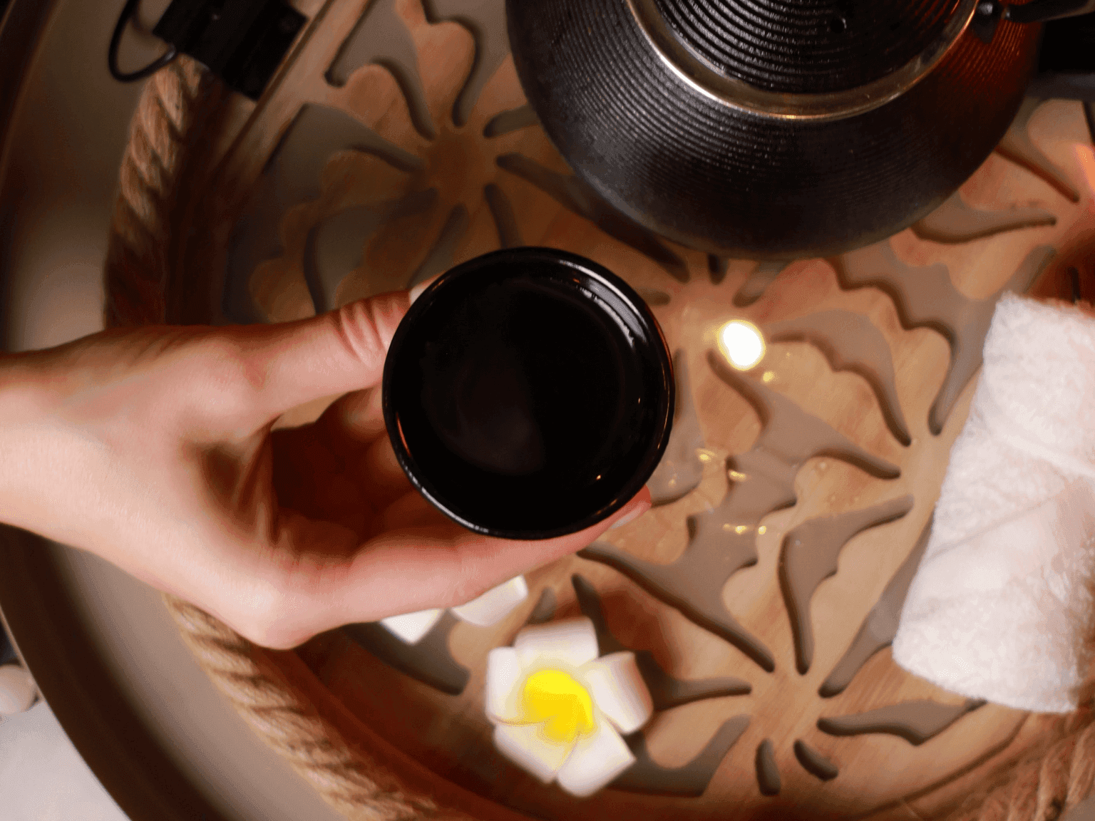 Guest holding warm cup of tea with floral decor and a calming tray arrangement in Dreamworks Spa at DAMAC Maison Distinction