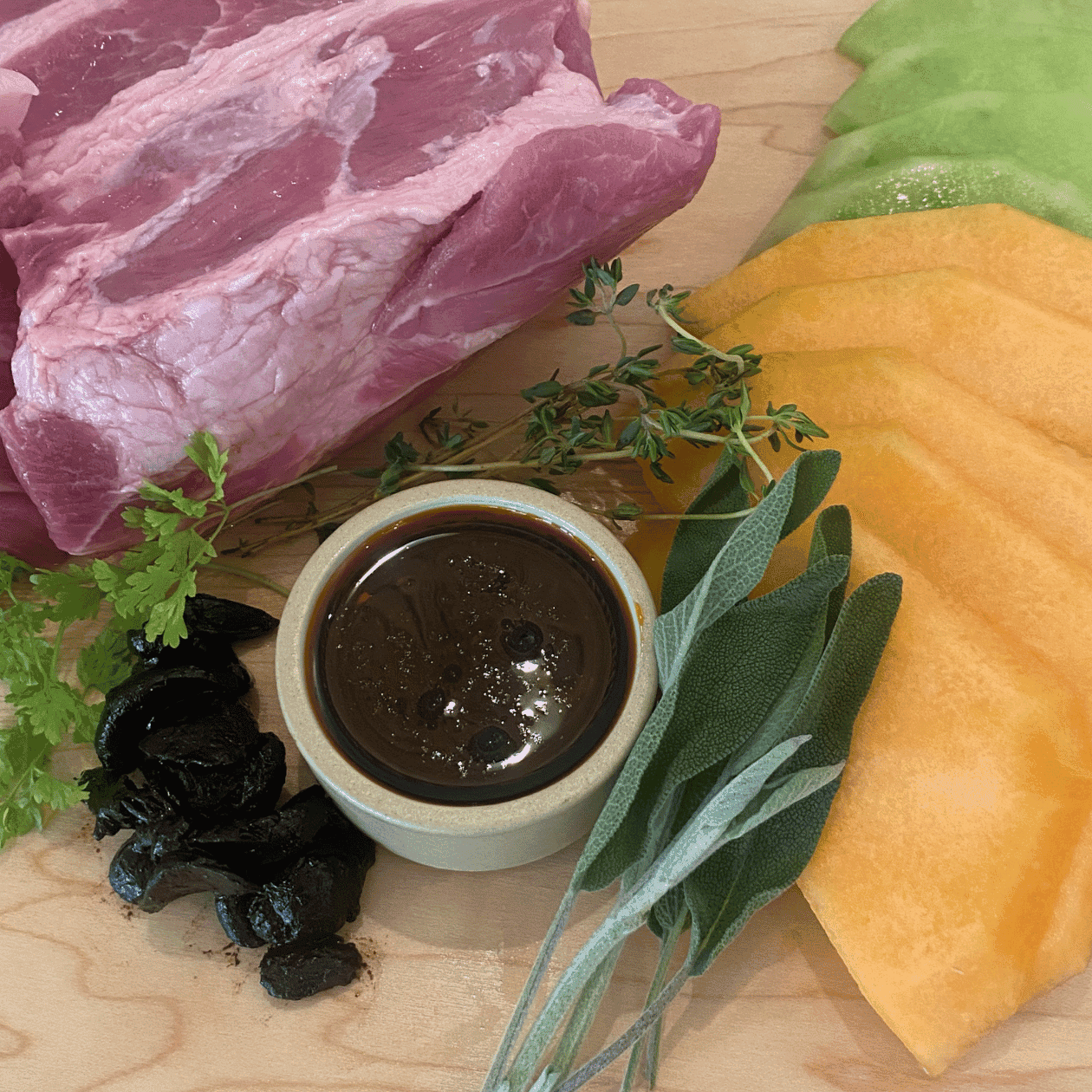 Raw meat, sauce, herbs, and black food item on a wooden surface.