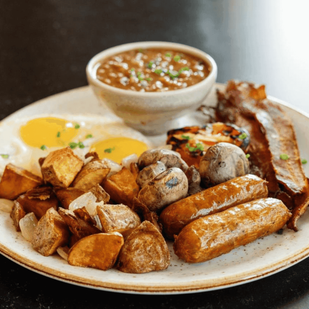 A Plate filled with diced potatoes, sausage links, bacon, eggs, and bowl of oatmeal