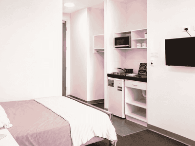 Modern student studio with pink and white decor, compact kitchenette, wall-mounted TV, and single bed at Student Living Waymouth