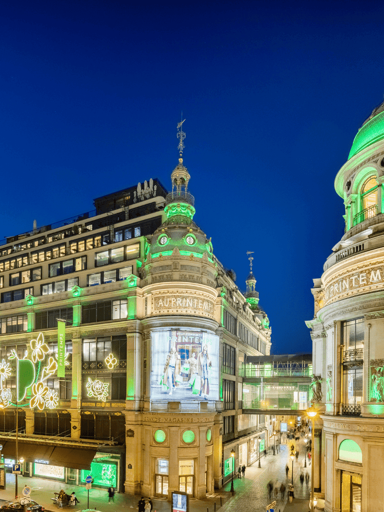 Printemps building facade illuminated with green lighting by street traffic near Hotel Westminster Paris
