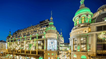Printemps building facade illuminated with green lighting by street traffic near Hotel Westminster Paris