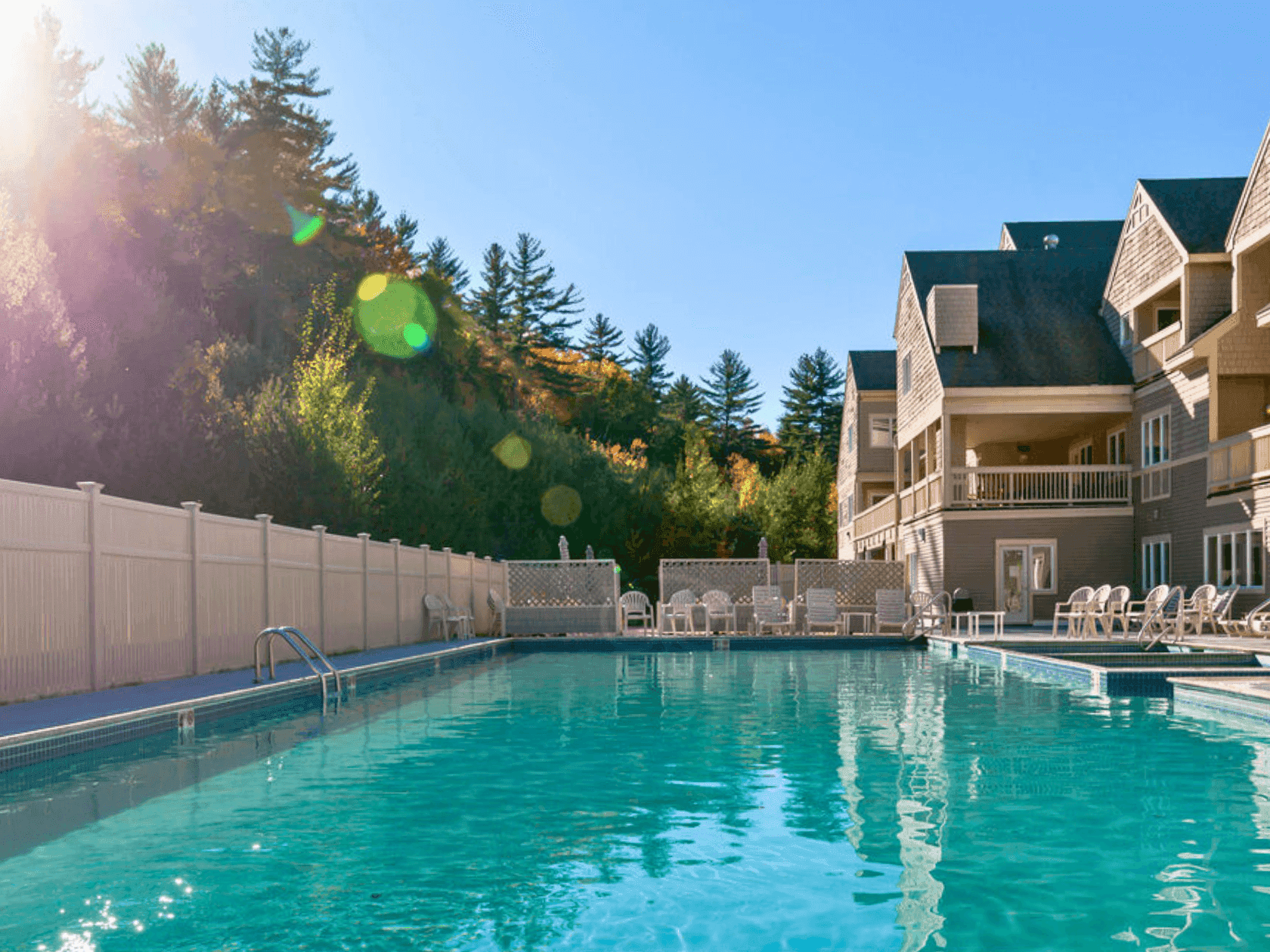 An outdoor pool with lounge chairs and buildings in the background under a bright sky.