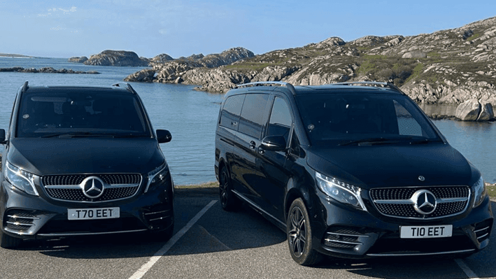 Two black Mercedes vans parked by the sea with rocky hills in the background near Seaton House