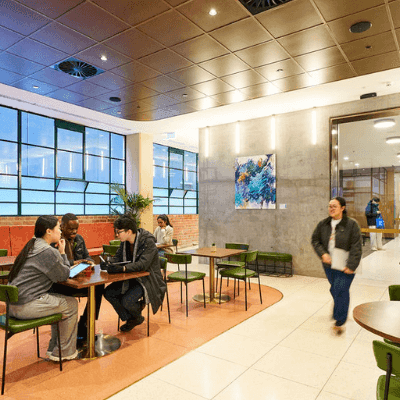 People sitting and walking in a cafe with large windows, art on the walls, and tables.