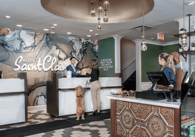 Hotel Saint Clair lobby with reception desks beside a cafe counter under pendant lights and a marble-patterned wall