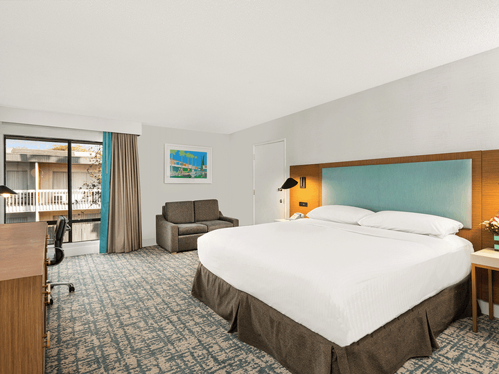 A hotel room with a large bed, desk, sofa, and sliding glass door