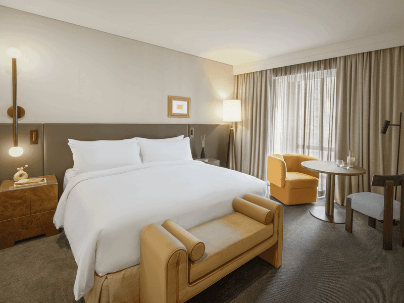 Modern hotel room featuring king bed with yellow accent pillows and wooden bench