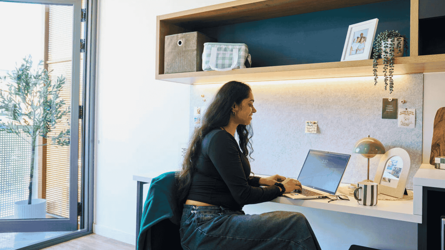 Woman working at a desk with laptop and balcony view at UniLodge Royal Melbourne.