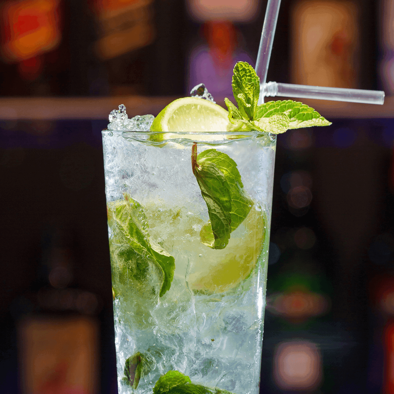 A cocktail glass with ice, lime slices, and mint leaves, topped with a straw.