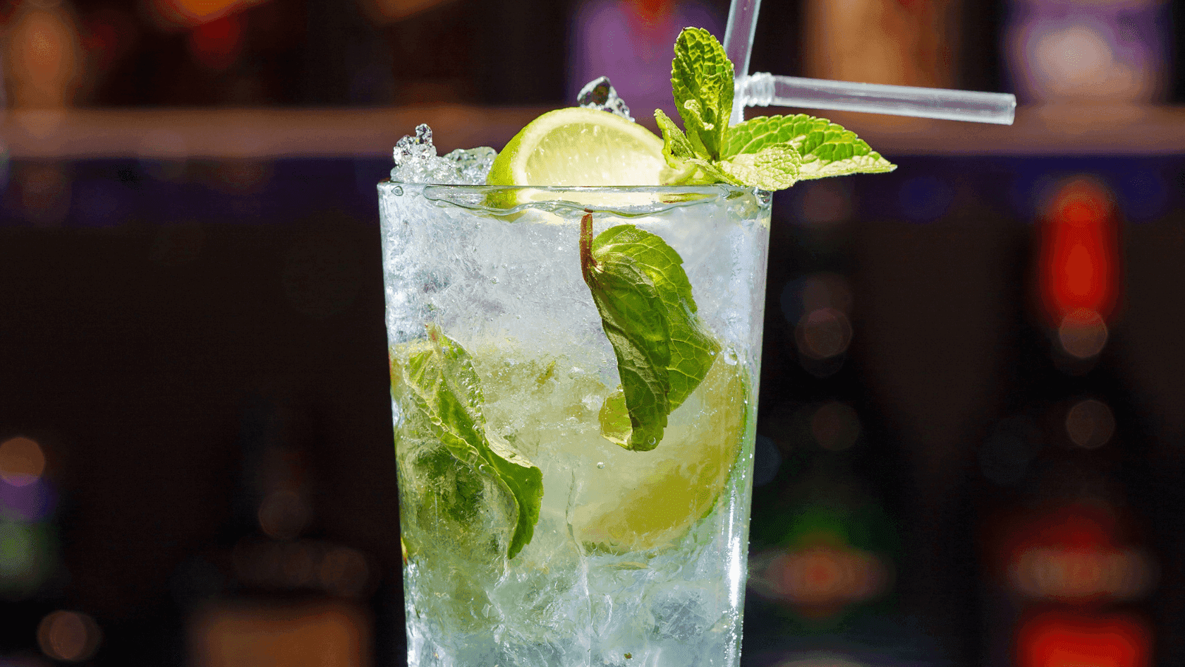 A cocktail glass with ice, lime slices, and mint leaves, topped with a straw.