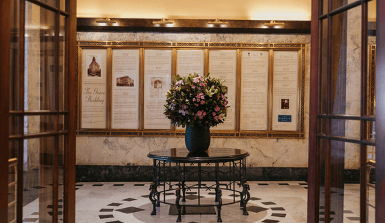 Lobby with a round iron table with flowers sits by a wall displaying the building's historic timeline at The Grace Sydney