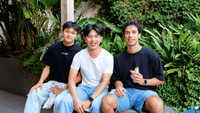 Three smiling students enjoying food together in a lush outdoor courtyard setting at UniLodge.