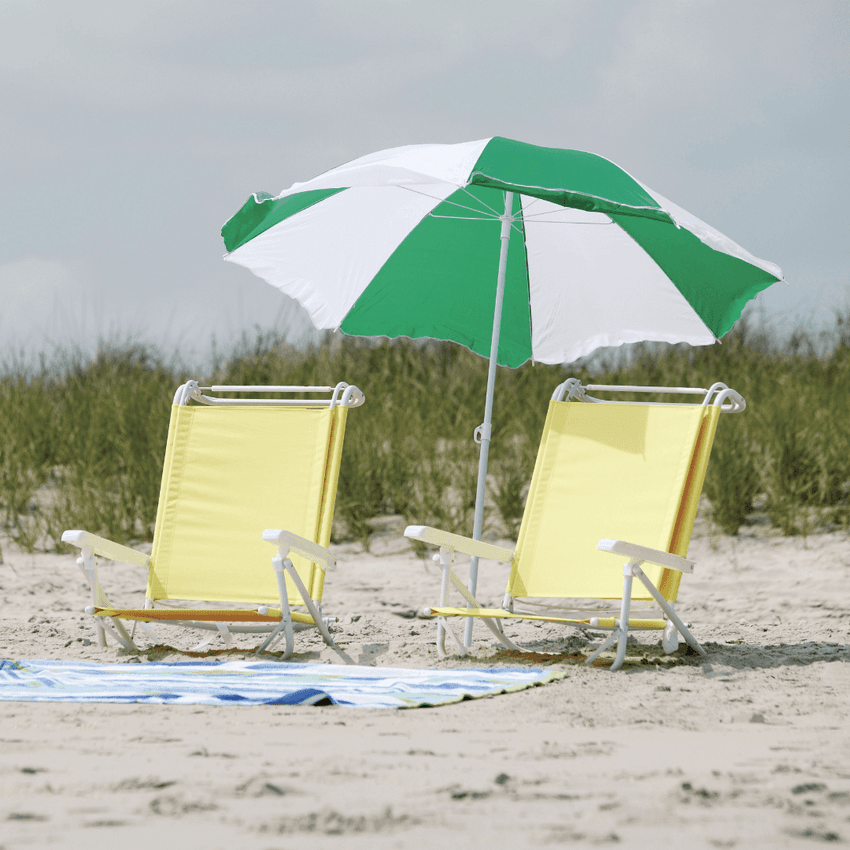 Two yellow beach chairs with a green and white umbrella on a sandy beach.